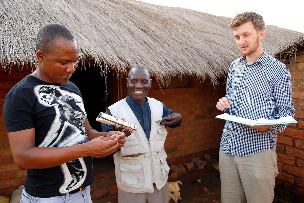Ser lyset: Landsbyhøvdingen (i midten) viser Thomas og hans kollega, elektroingeniøren Geoffrey, hva slags batteri han bruker til lys. Han ønsker seg solceller i landsbyen.  